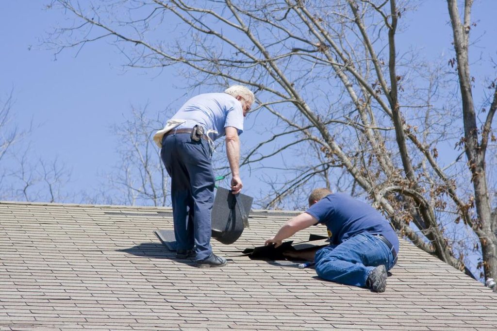Two men working to repair a roof leak with some new shingles For Delaware County Roofers
